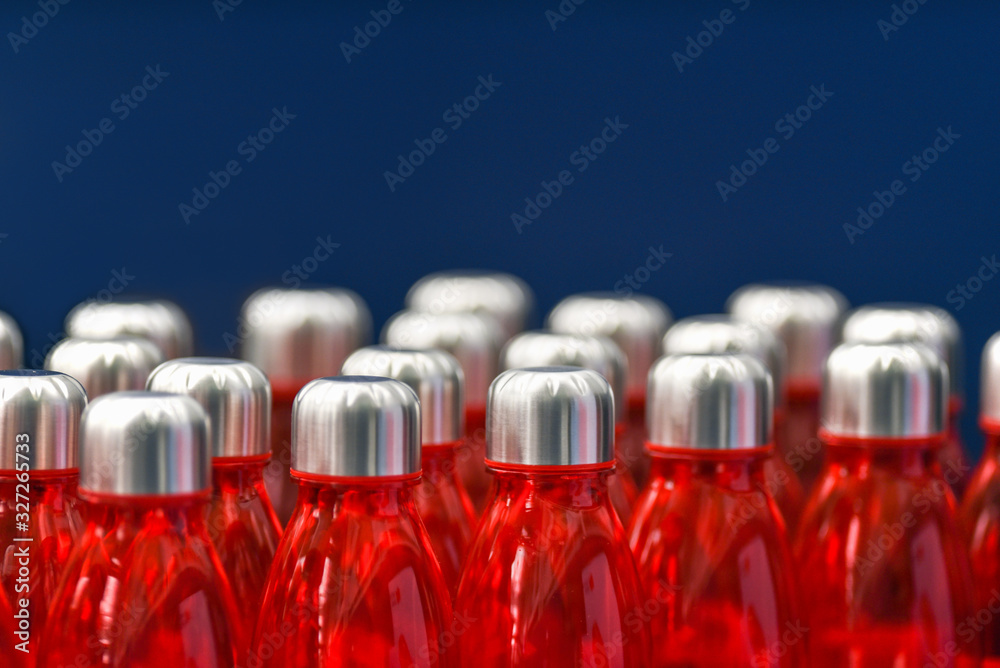 Red water bottles with silver metallic caps in rows isolated on blue background